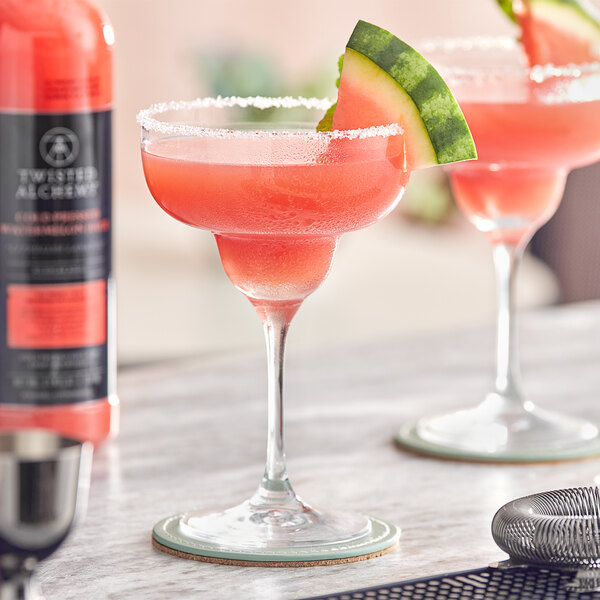 Two glasses of Twisted Alchemy watermelon juice on a table with slices of watermelon.