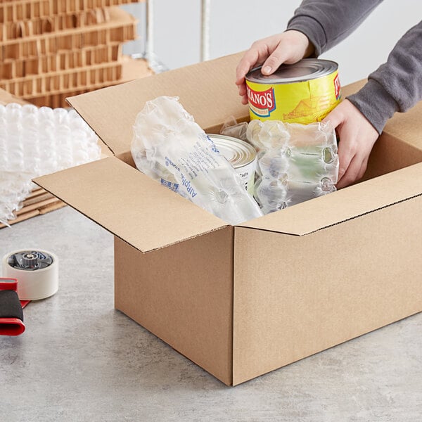 A person holding a can of chips and putting it in a Lavex kraft cardboard shipping box.