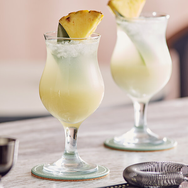 Two glasses of Twisted Alchemy pineapple drinks on a table with pineapple garnish.