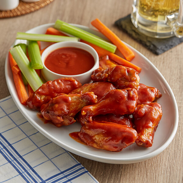 A plate of chicken wings with French's BBQ sauce, carrots, and celery.