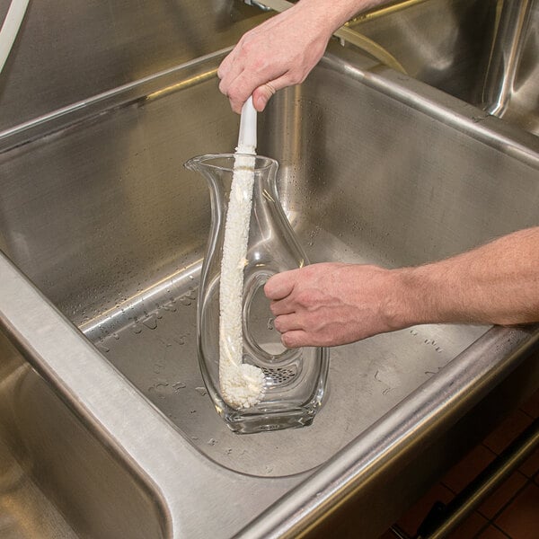 A hand using a Franmara wine decanter brush to clean a glass pitcher.