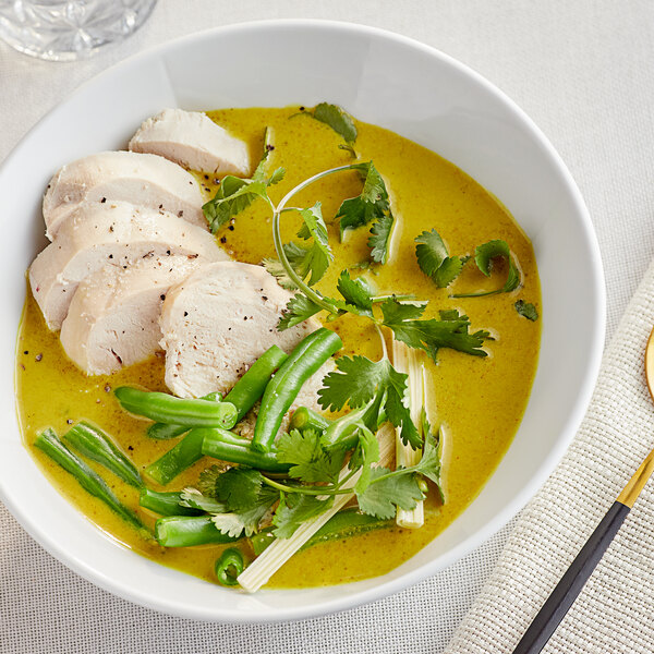 A bowl of curry soup with chicken and vegetables.