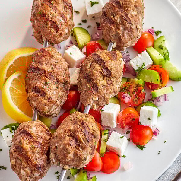 A plate of meat skewers with tomatoes and cucumbers on a white surface.