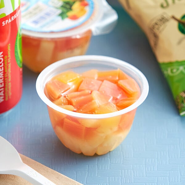 A white plastic spoon next to a plastic container of Dole tropical fruit.