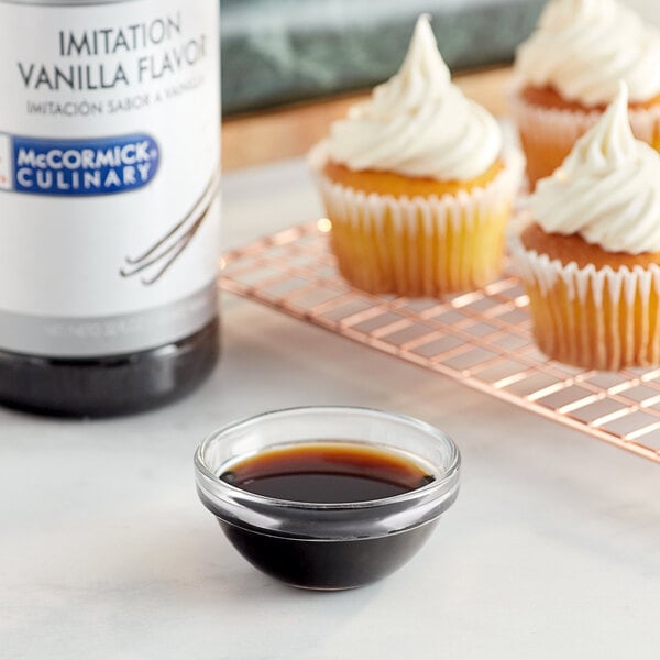 A cupcake with white frosting next to a bowl of McCormick Culinary Imitation Vanilla.