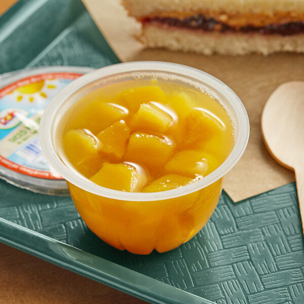 A plastic container holding a Dole Diced Mango cup next to a sandwich.