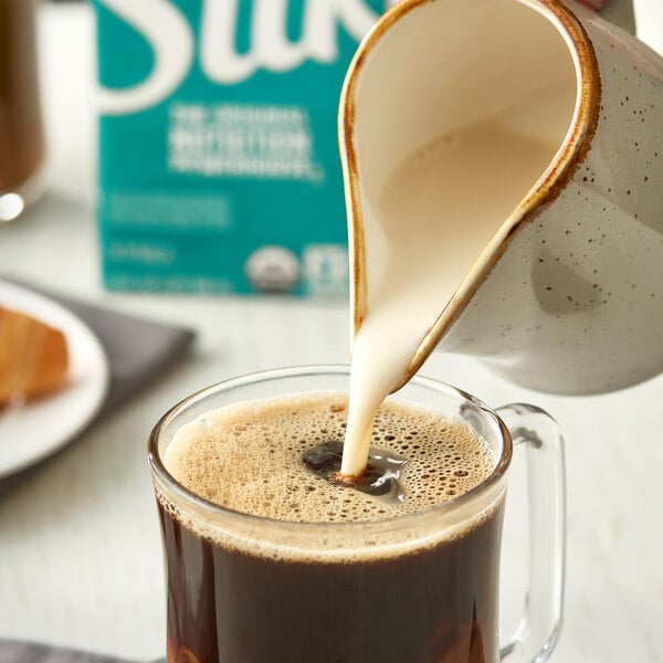 A person pouring Silk Organic Unsweetened Soy Milk into a glass of coffee.