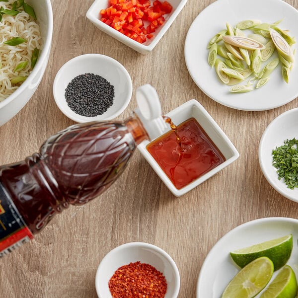 A bottle of THAI Kitchen Premium Fish Sauce pouring into a bowl of noodles with green onions and red peppers.