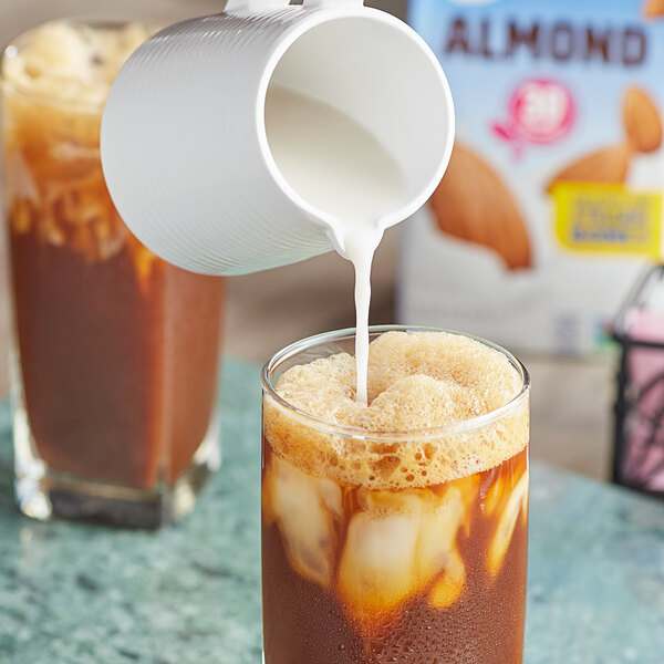 Silk Unsweetened Vanilla Almond Milk being poured into a white cup of iced coffee.