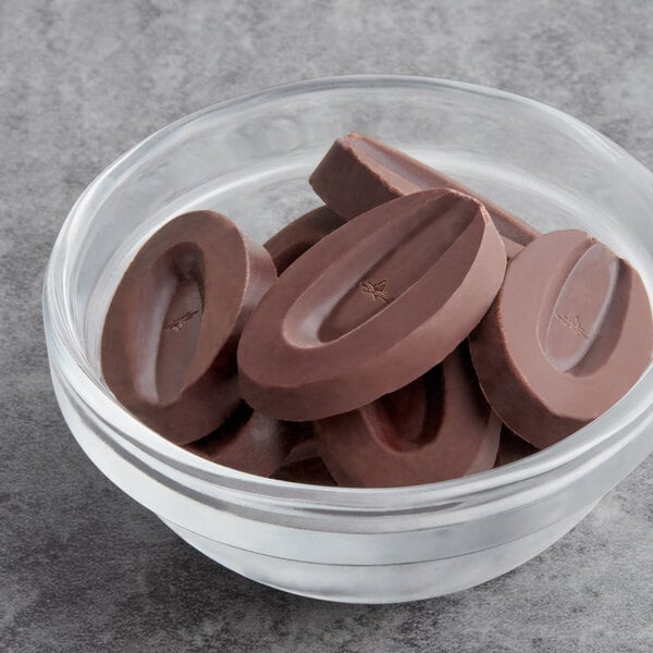 A glass bowl of Valrhona Guanaja dark chocolate feves on a gray surface.