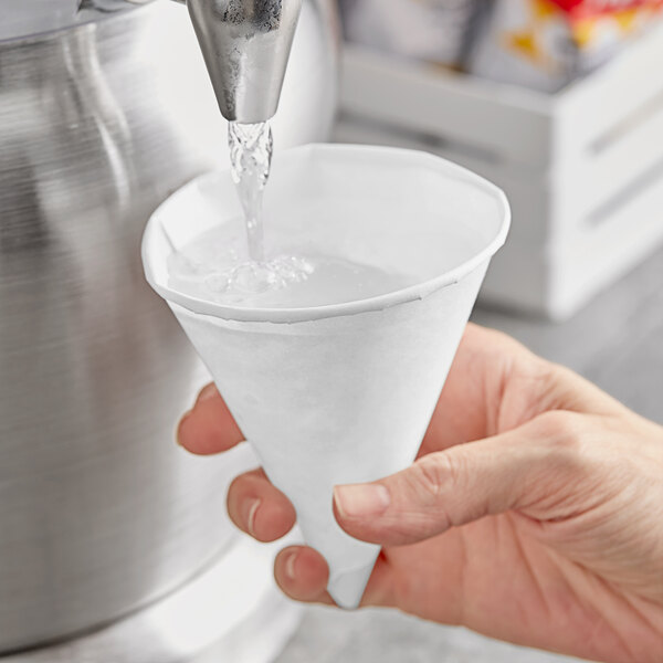 A hand pouring water into a Choice white paper cone cup.