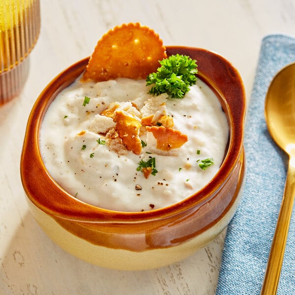 A bowl of clam chowder with crackers and parsley.