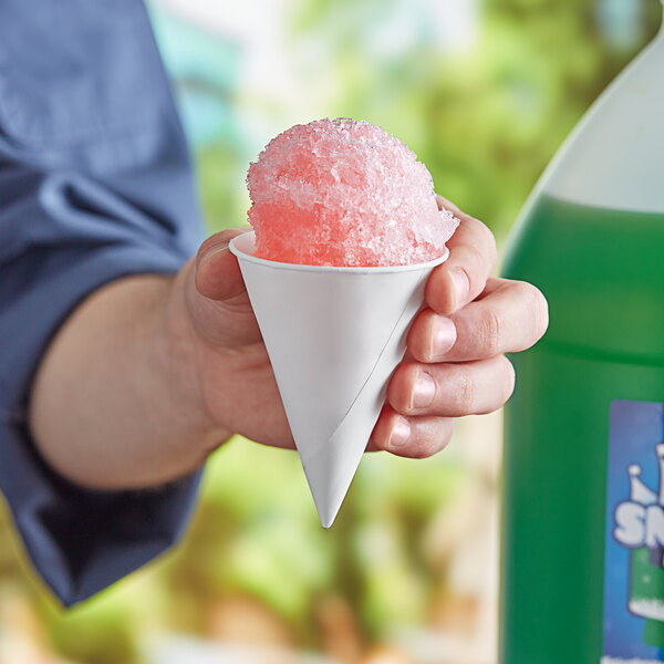 A person holding a white Choice paper cone with pink snow on it.