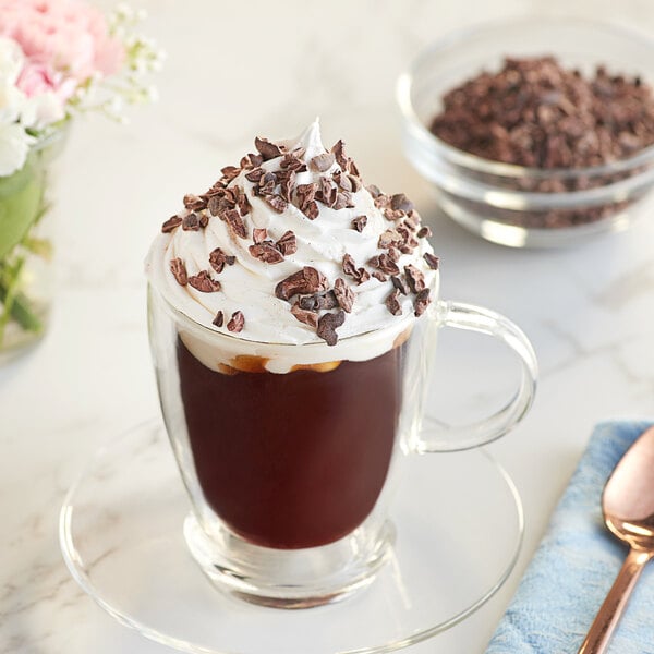 A glass cup of coffee with whipped cream and Republica del Cacao Vinces cacao nibs.
