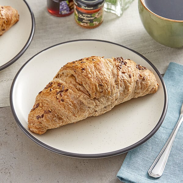 Two multigrain croissants on a plate with coffee and a spoon.