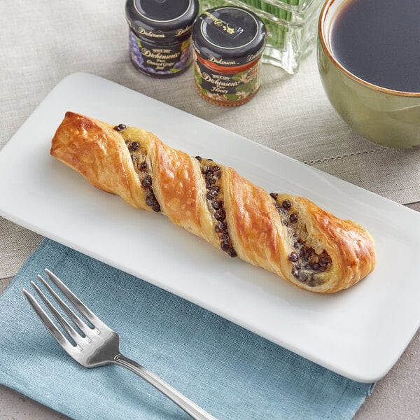 A Gourmand chocolate custard butter twist pastry on a plate next to a fork and a cup of coffee.