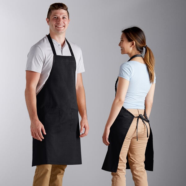 A man and woman standing on either side of a counter, both wearing black Choice standard bib aprons.