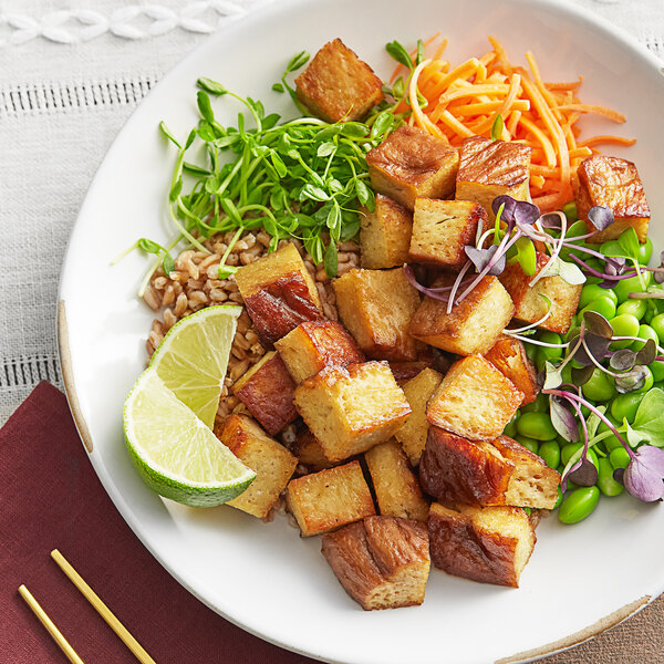 A plate of food with Blackbird Foods seitan, rice, and vegetables with a lime wedge.