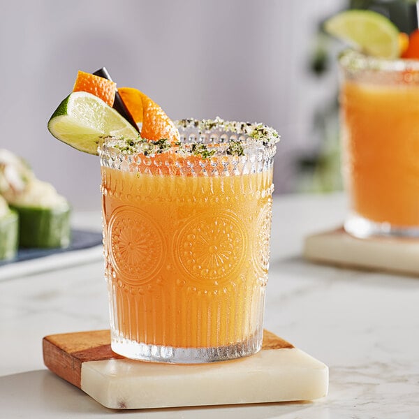 A glass of orange juice with a slice of orange and a lime on a marble coaster.