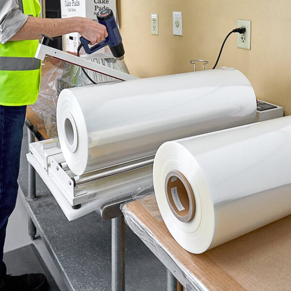 A person in a yellow vest using a machine to roll Lavex Pro 20" Polyolefin Shrink Film.