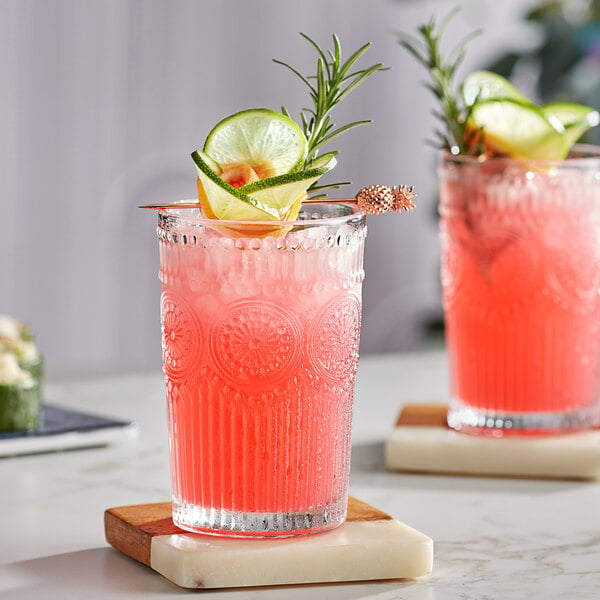 Two Acopa Esme highball glasses filled with red drinks garnished with rosemary on a table in a cocktail bar.