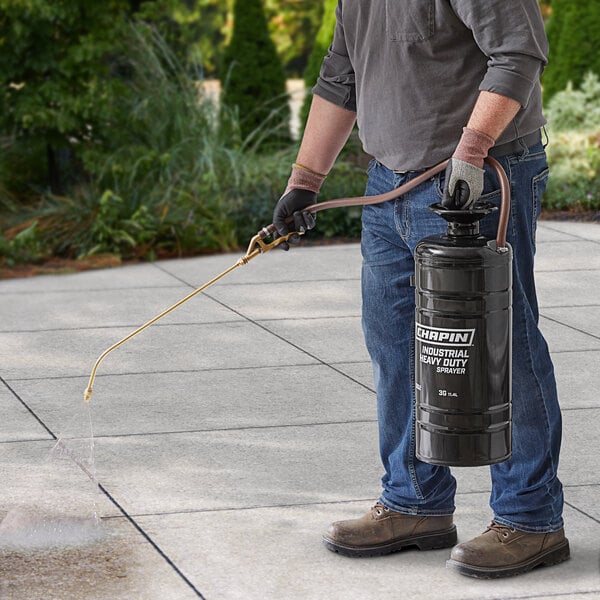 A man using a Chapin metal sprayer to spray a garden hose.