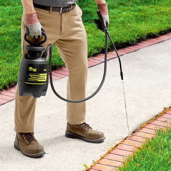 A man using a black Chapin Poly Foamer / Sprayer to spray a sidewalk.