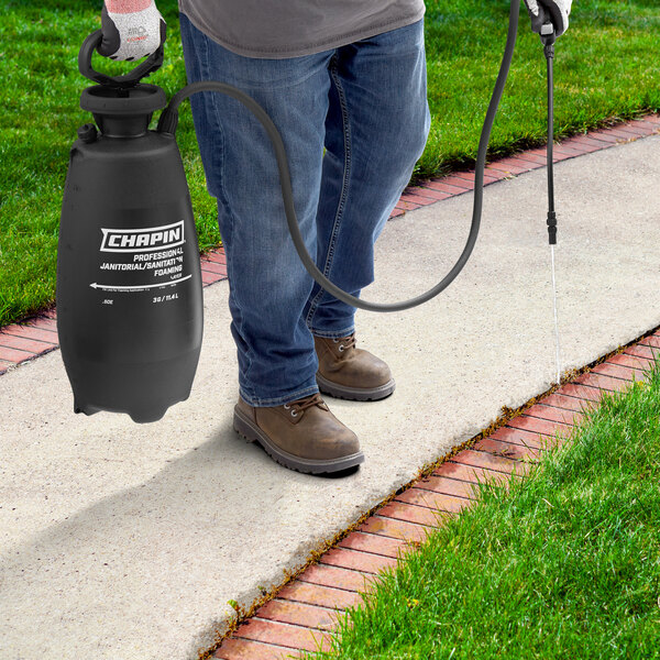 A man using a Chapin 3 gallon black and white sprayer on a lawn.