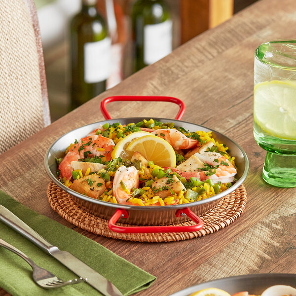 A Vigor paella pan with shrimp, lemons, and rice on a table.