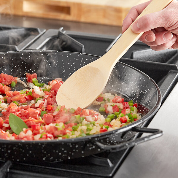 A person stirring paella in a Vigor enameled carbon steel pan with a wooden spoon.
