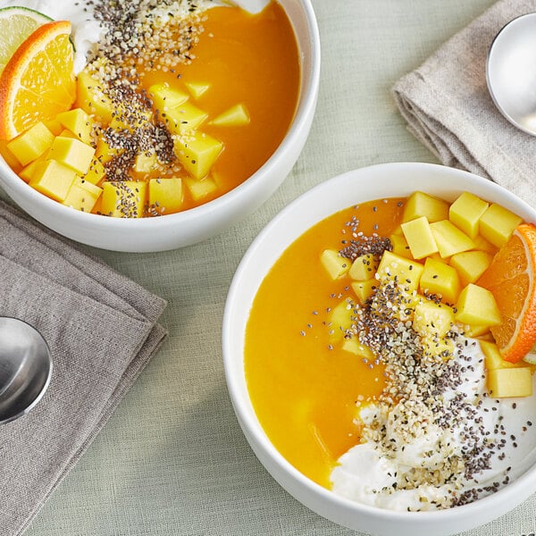 A white bowl of fruit and yogurt next to a white bowl of fruit and cream.