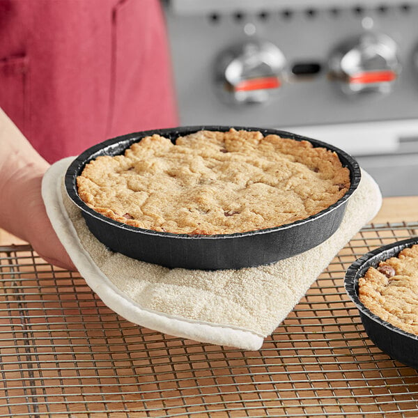 A person holding a Solut round black paperboard pan with a pie inside.