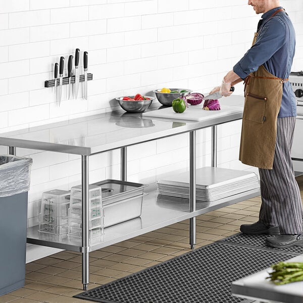 A man cutting vegetables on a Regency stainless steel work table in a professional kitchen.