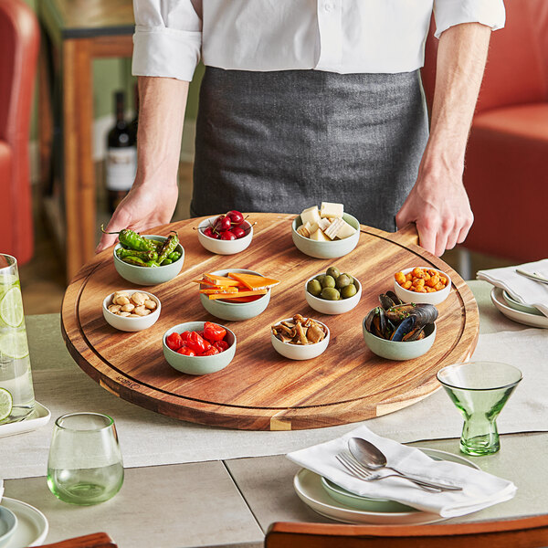 A waiter holding an Acopa acacia wood serving board with food on a table.