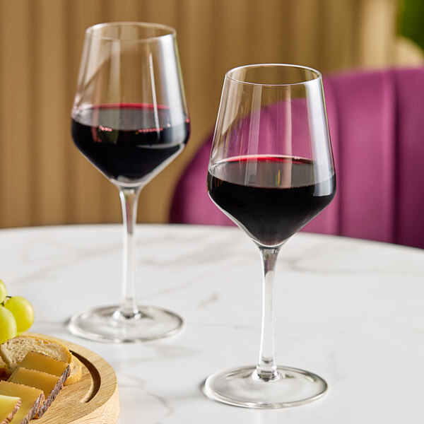 Two Acopa Silhouette wine glasses filled with red wine on a table.