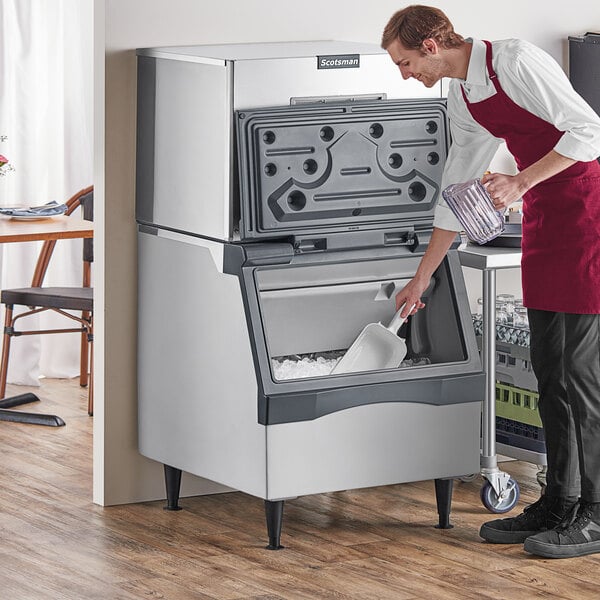 A man in an apron standing next to a Scotsman air cooled ice machine, putting ice into a plastic container.