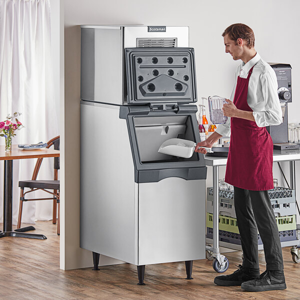 A man in a red apron standing next to a Scotsman air cooled ice machine.