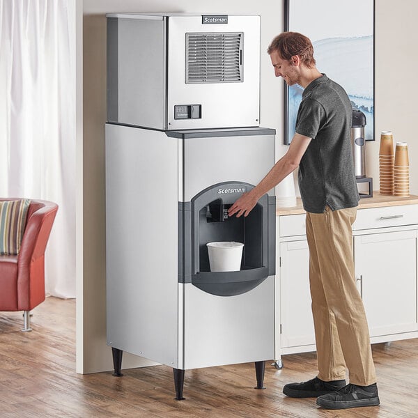 A man standing in front of a Scotsman small cube ice machine and dispenser reaching to pour water into it.