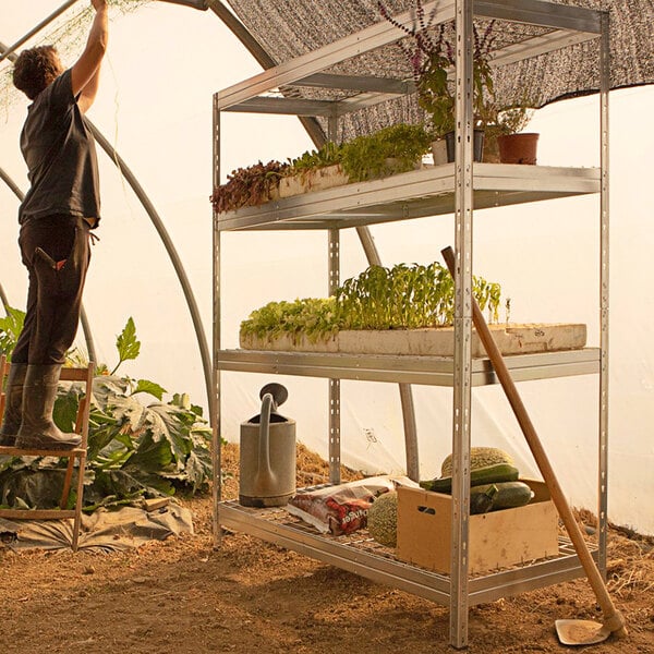 A man assembling an AR Shelving galvanized boltless wire shelving unit in a greenhouse.