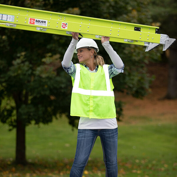 A woman wearing a safety vest and white helmet holding a yellow Bauer Corporation FiberLite professional grade extension ladder.