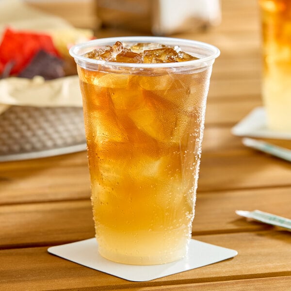 A clear plastic cup filled with iced tea and ice cubes, placed on a white coaster.
