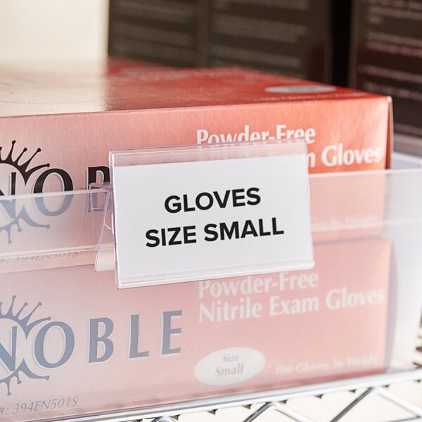 A close-up of a small label holder clipped on a shelf with a box of small gloves inside.