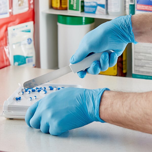 A person in a blue Showa nitrile glove cuts food with a knife.