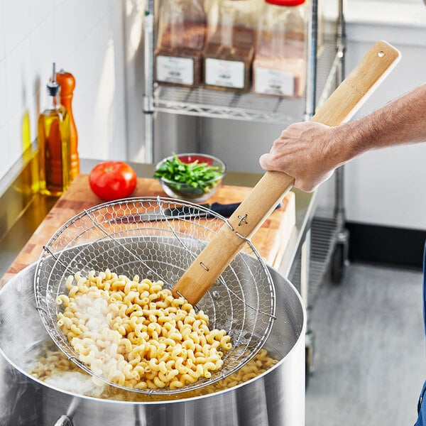 A person using Emperor's Select coarse skimmer with a bamboo handle to stir a pot of food.