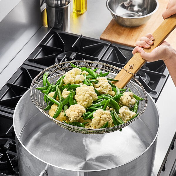 A person using Emperor's Select fine skimmer to remove vegetables from a pot.