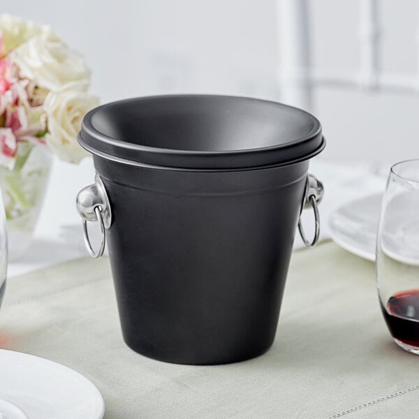 An Acopa black stainless steel wine tasting spittoon on a table.