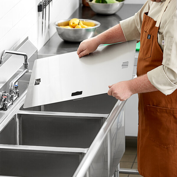 A man in brown overalls holding a Regency stainless steel sink cover over a counter with bowls of yellow pears.