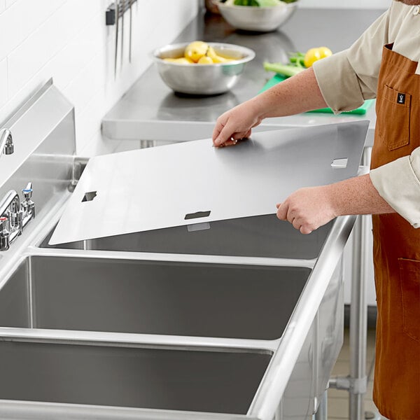 A person in an apron placing a metal lid on a sink.