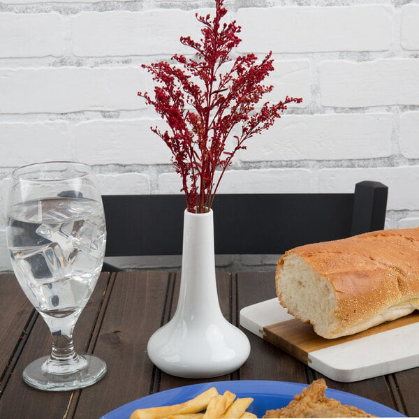 A white CAC porcelain bud vase with red flowers on a table.