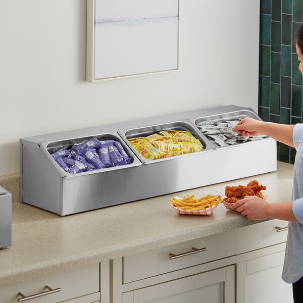 A woman using a ServSense stainless steel hotel pan organizer with condiments in it.